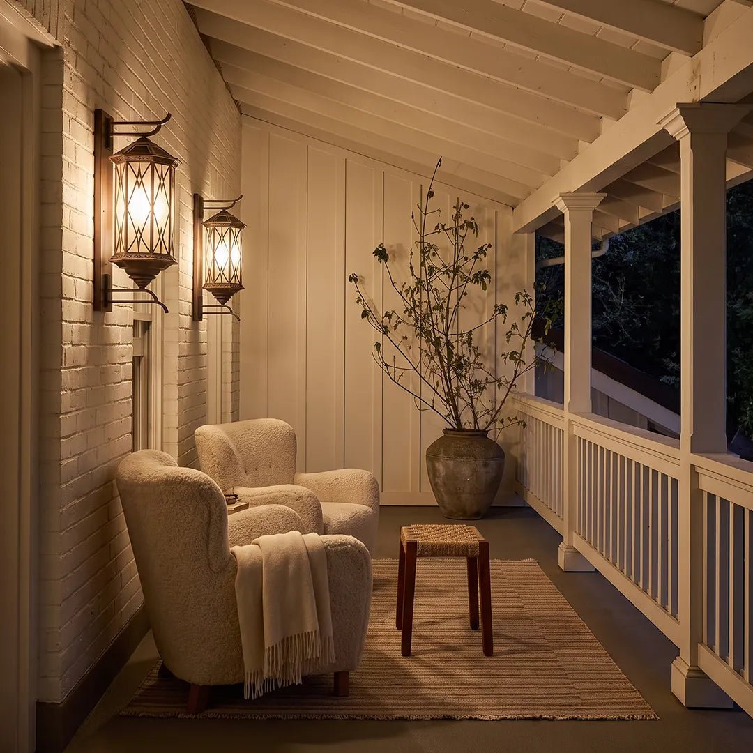 Bronze outdoor sconce installed along a covered porch, bringing warm ambient lighting to the outdoor seating area.