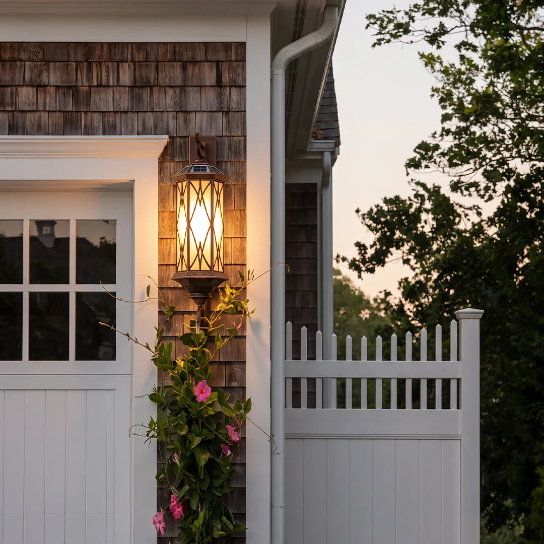 Bronze outdoor sconce installed beside a fence gate and window, providing elegant outdoor lighting at dusk.