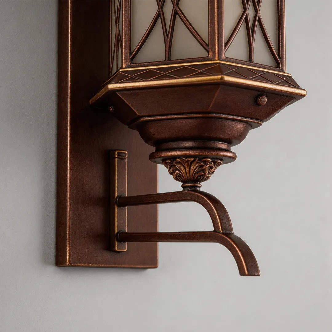 Bronze outdoor sconce close-up highlighting the lower lantern base, curved arm, and decorative metal detailing.