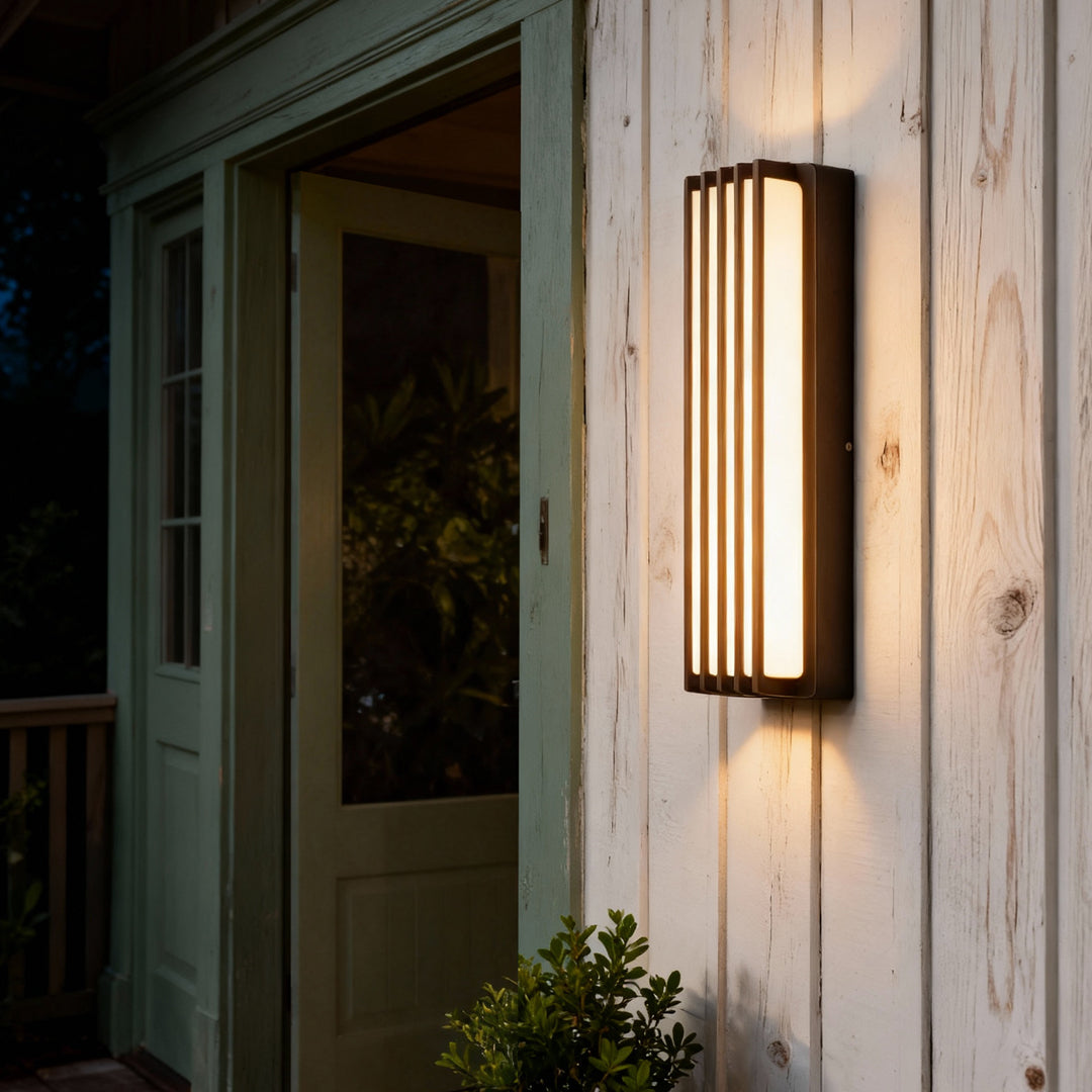 Tall bronze wall-mounted linear lighting illuminating a wooden exterior wall in a contemporary outdoor setting.