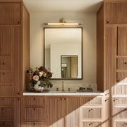 Brushed gold vanity light bar mounted above a bathroom mirror in a warm wood vanity space.