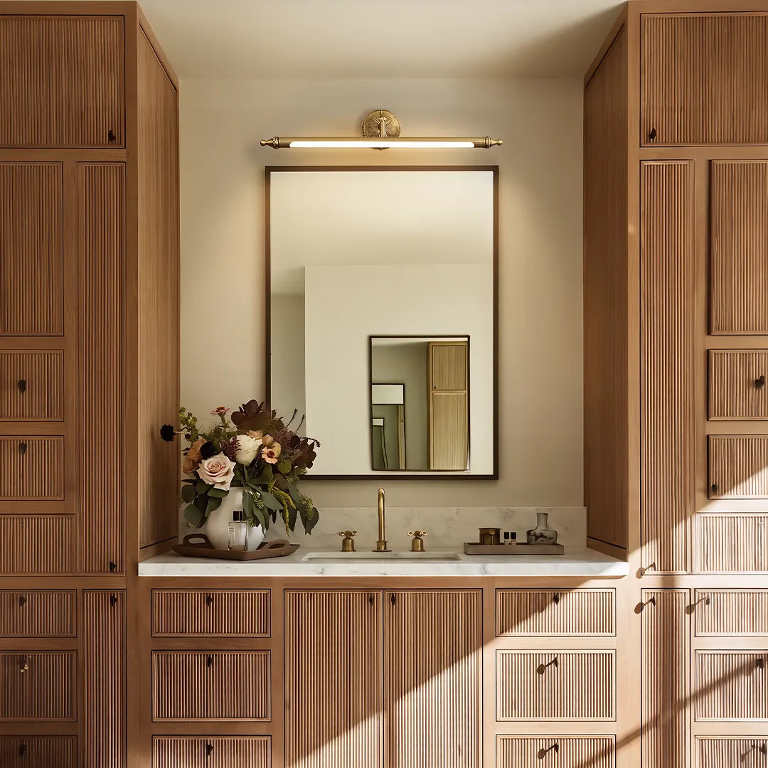Brushed gold vanity light bar mounted above a bathroom mirror in a warm wood vanity space.