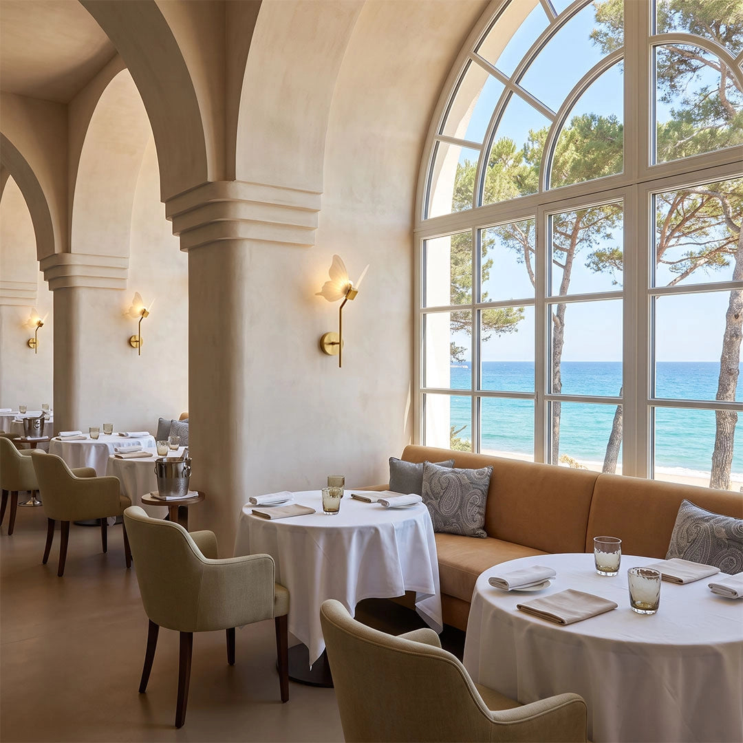Butterfly wall light installed in an elegant dining space with arched windows and ocean views.