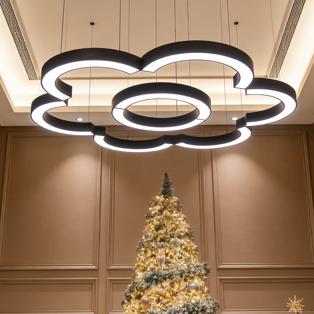 C shape LED pendant light hanging above Christmas tree in modern interior space.