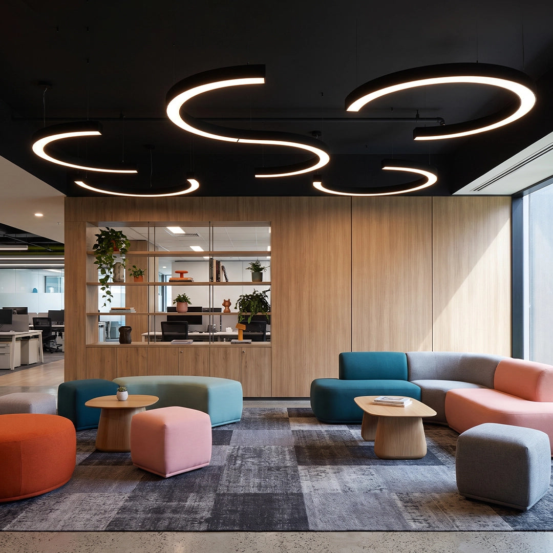 C shape pendant light in a contemporary lounge area, with layered circular LED pendant rings over colorful seating.