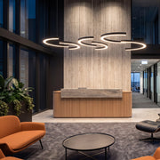 C shape pendant light in a modern office lobby, featuring multiple suspended LED ring segments above a wood reception desk.