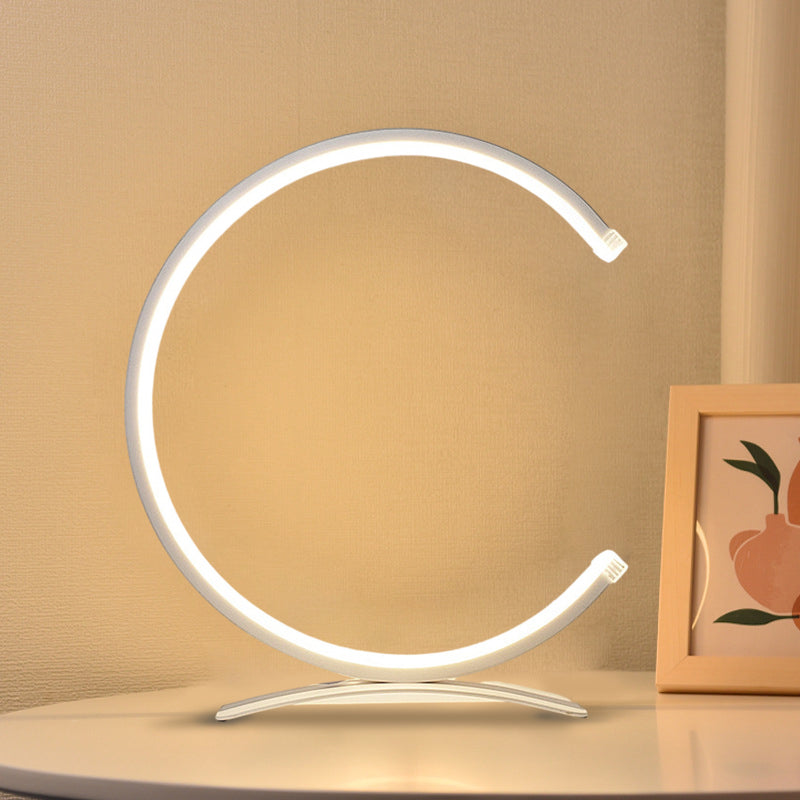C shaped table lamp casting a gentle glow on a white desk setup.
