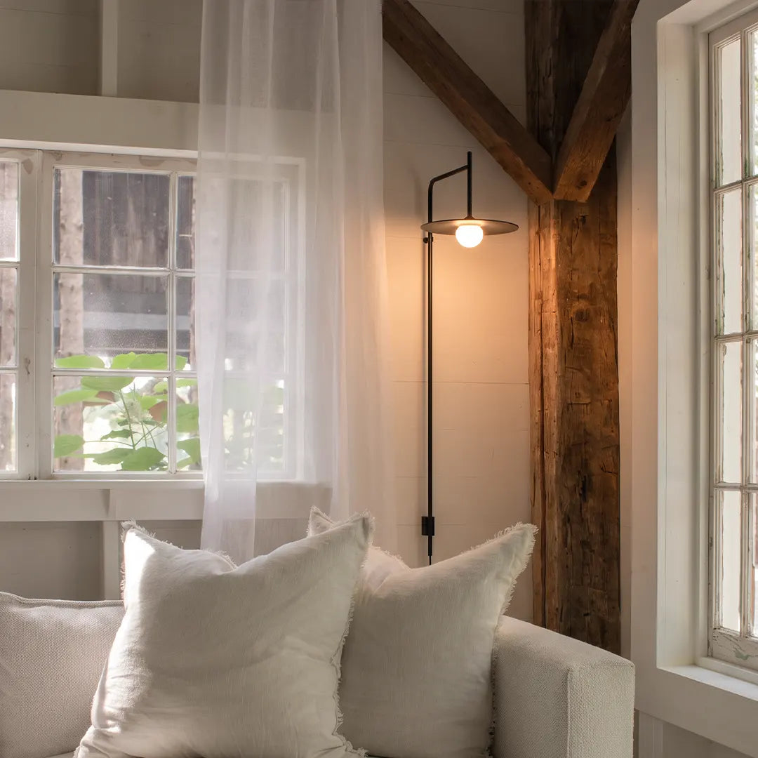 Cantilever wall lamp mounted beside a window, adding warm light to a soft neutral seating corner.