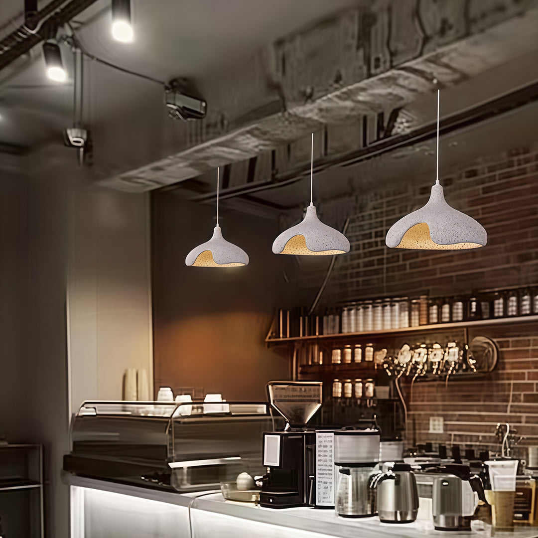 Cement Pendant Lights hanging above bar counter in café interior, creating warm industrial ambiance.