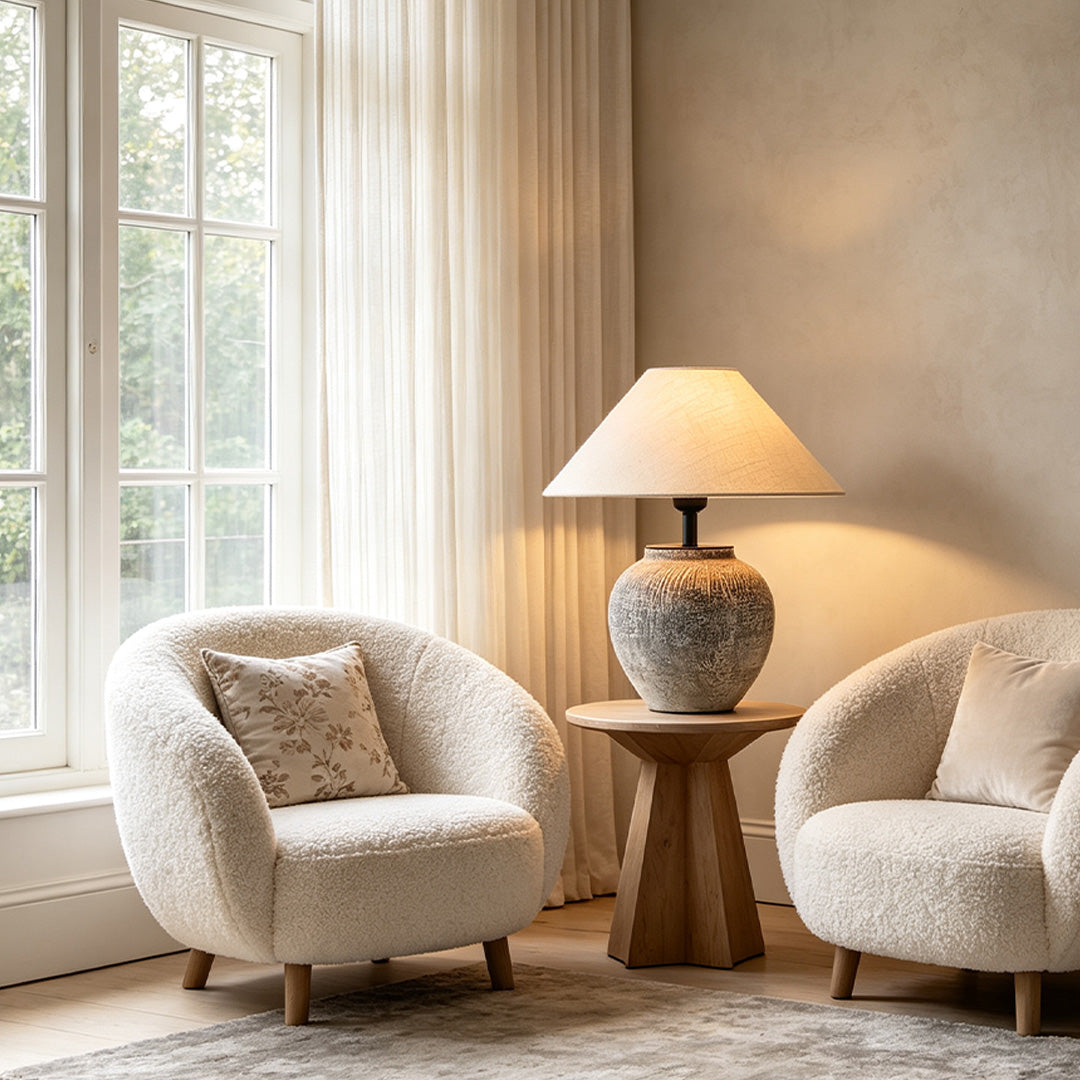 Ceramic base table lamp placed between two boucle accent chairs in a bright and airy sitting area.