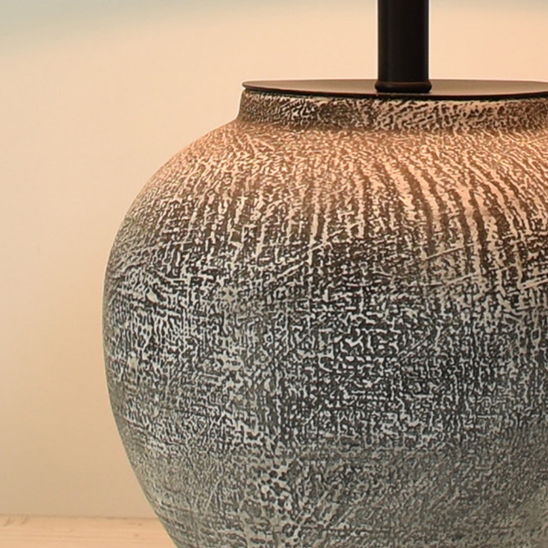 Close-up detail of a ceramic base table lamp showing the textured gray finish and rounded sculptural form.