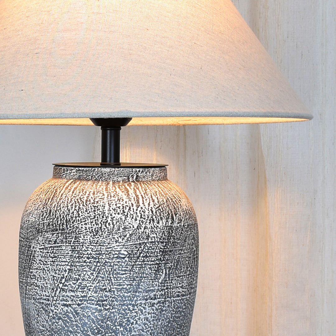 Close-up of a ceramic base table lamp highlighting the tapered fabric shade and textured ceramic body.