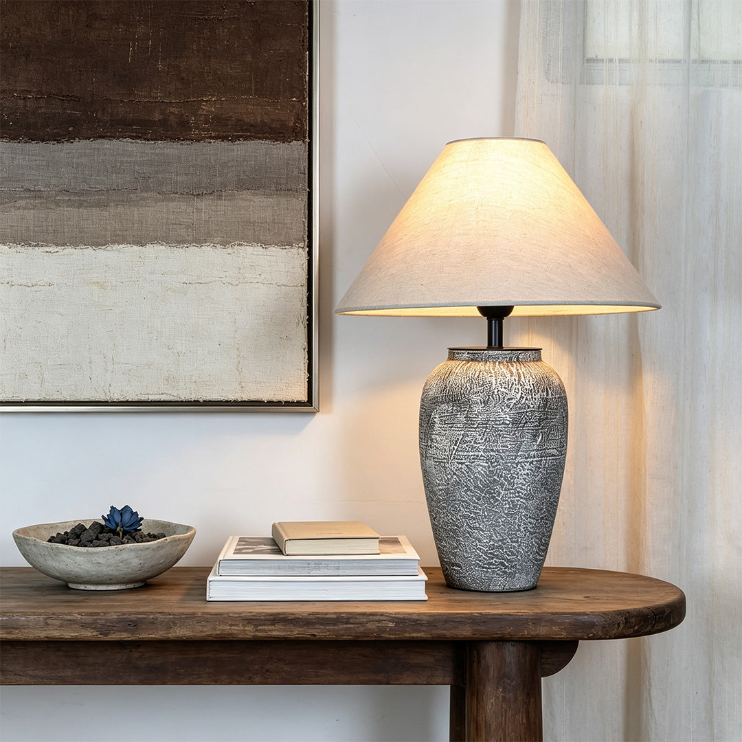 Ceramic base table lamp displayed on a round wood table with books and decor in a warm living room corner.