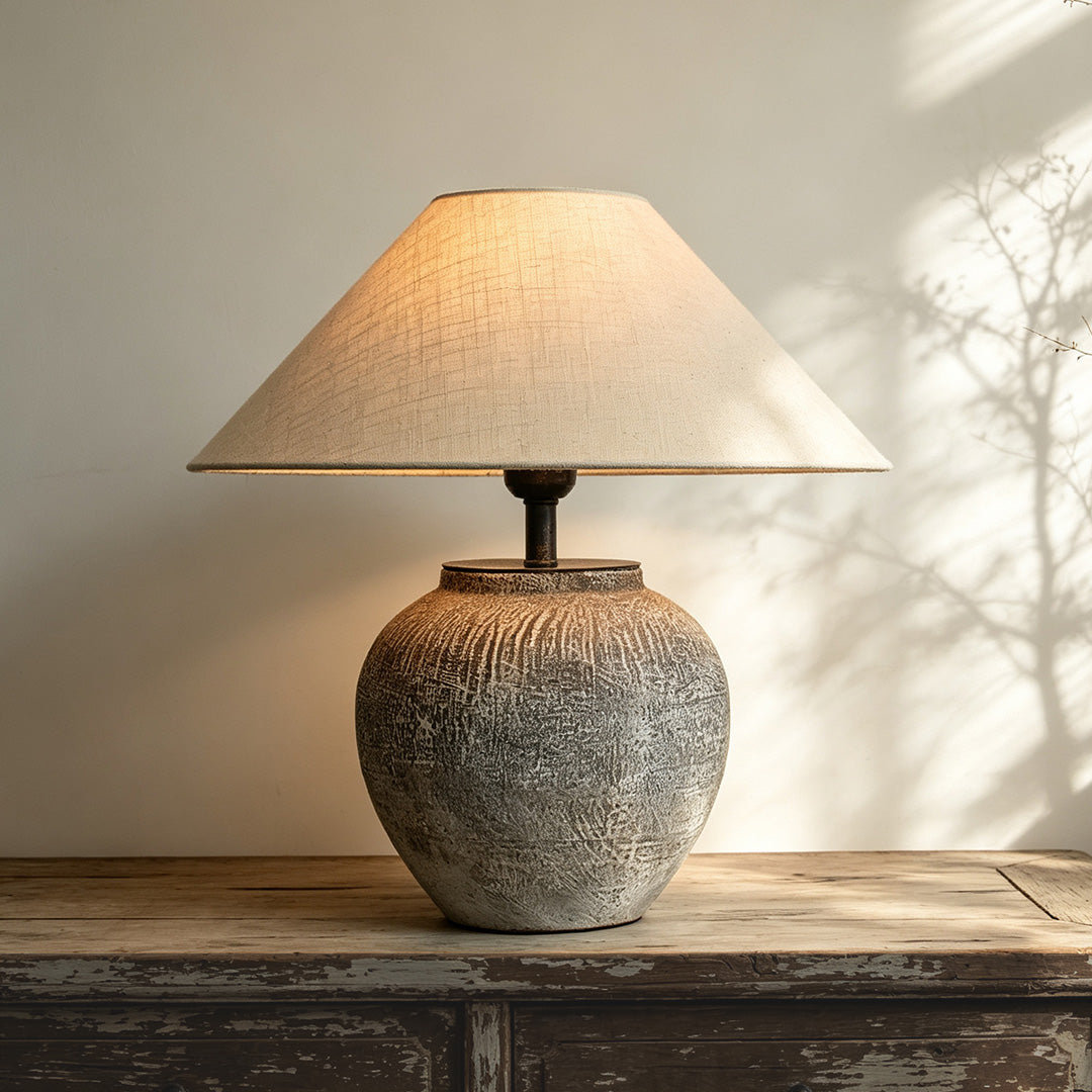 Ceramic base table lamp on a rustic wood console table, showing a rounded textured base and wide fabric shade.