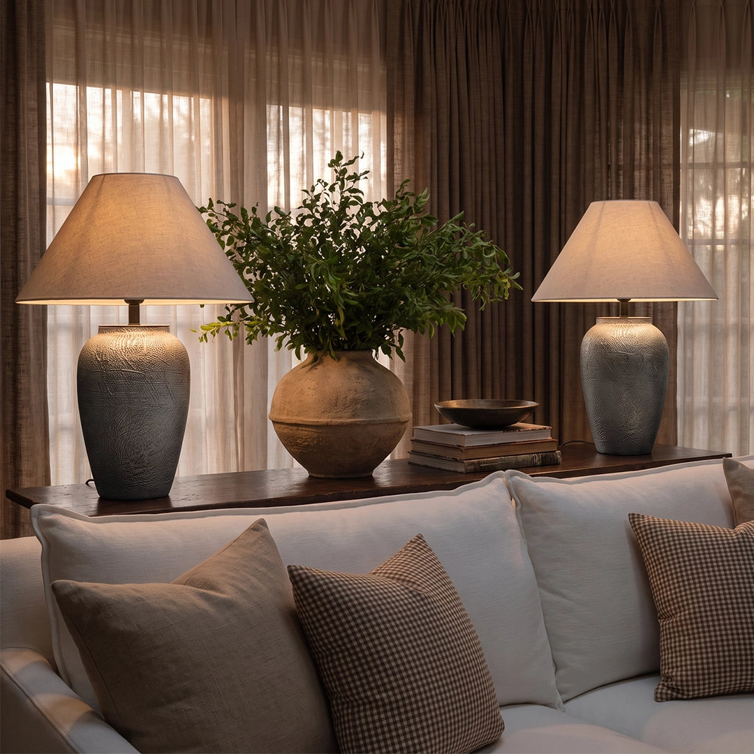 Two ceramic base table lamps styled behind a sofa, adding warm ambient lighting to a cozy living room.