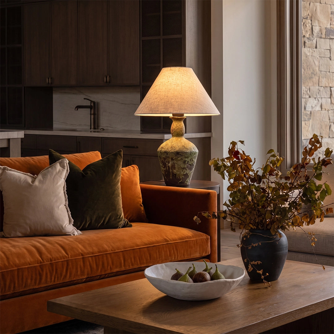 Ceramic bedside table lamp placed beside a warm-toned sofa, featuring a textured ceramic base and tapered fabric shade.
