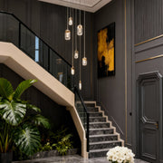 Chandelier for staircase descending along dark feature wall beside modern staircase with greenery accent at base