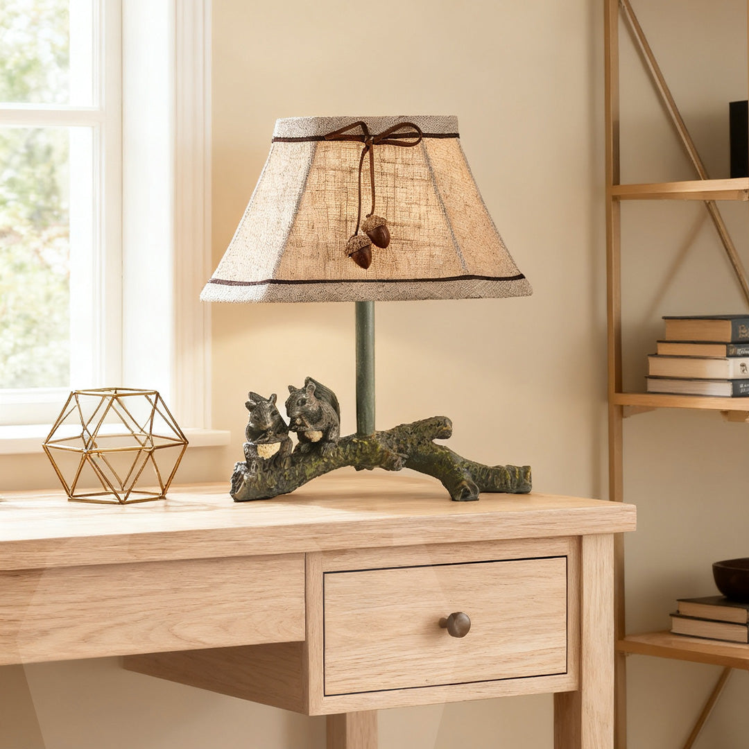 Charming squirrel table lamp highlighting the acorn-adorned shade, sitting on a light wood desk next to a window.
