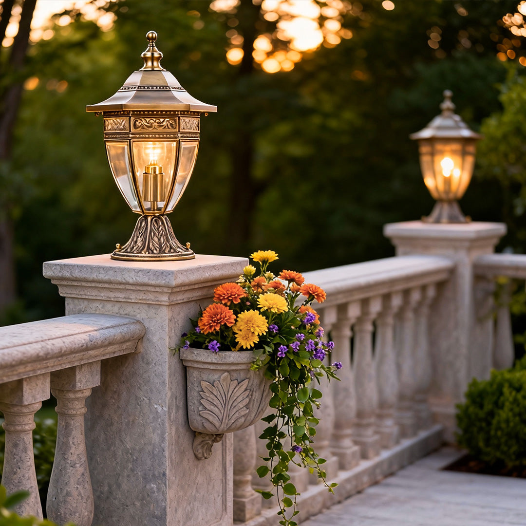 Charming glass pillar light with gold details, placed on a stone fence, creating a welcoming glow for outdoor spaces.