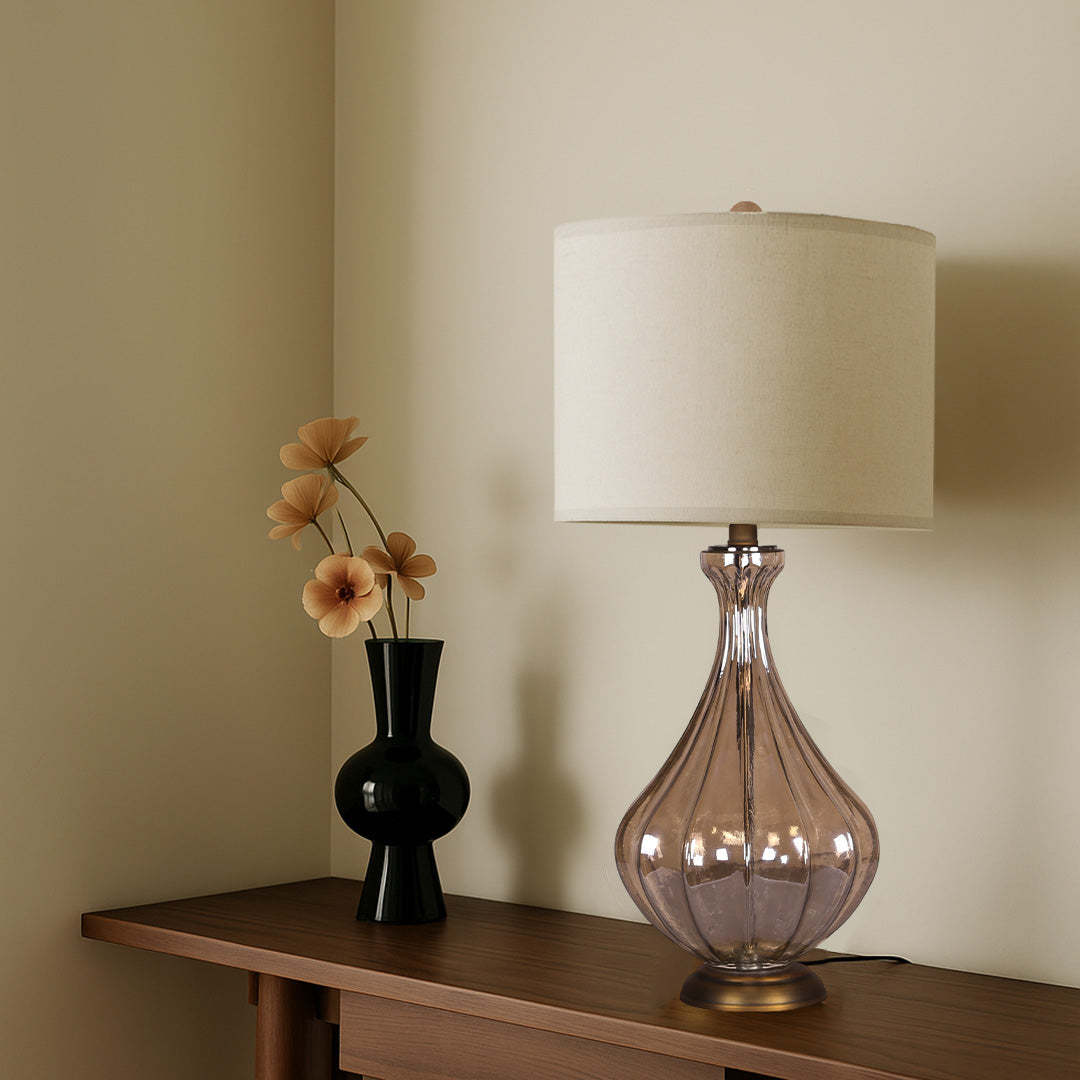 Chic bell-shaped glass base table lamp with a neutral textured shade, brightening a cozy corner with minimalist accessories.