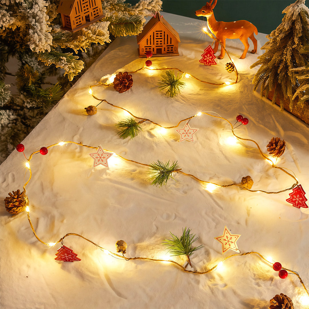 Warm white Christmas LED string lights set on a snowy scene with pinecones and miniature Christmas house.