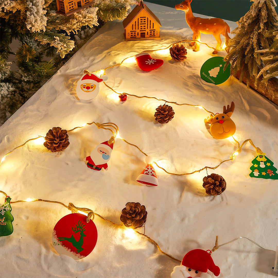 Warm white Christmas LED string lights set on a snowy scene with pinecones and miniature Christmas house.