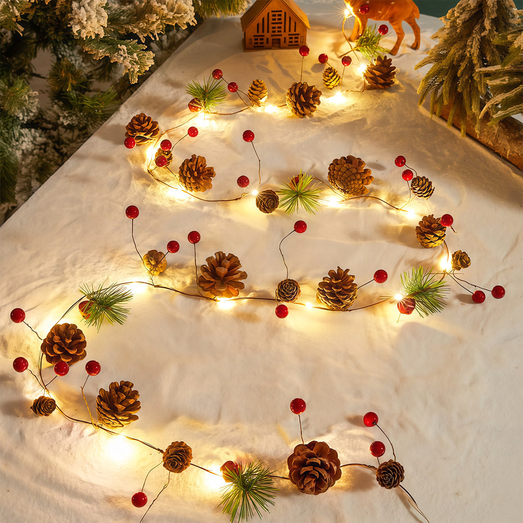 Warm white Christmas LED string lights set on a snowy scene with pinecones and miniature Christmas house.
