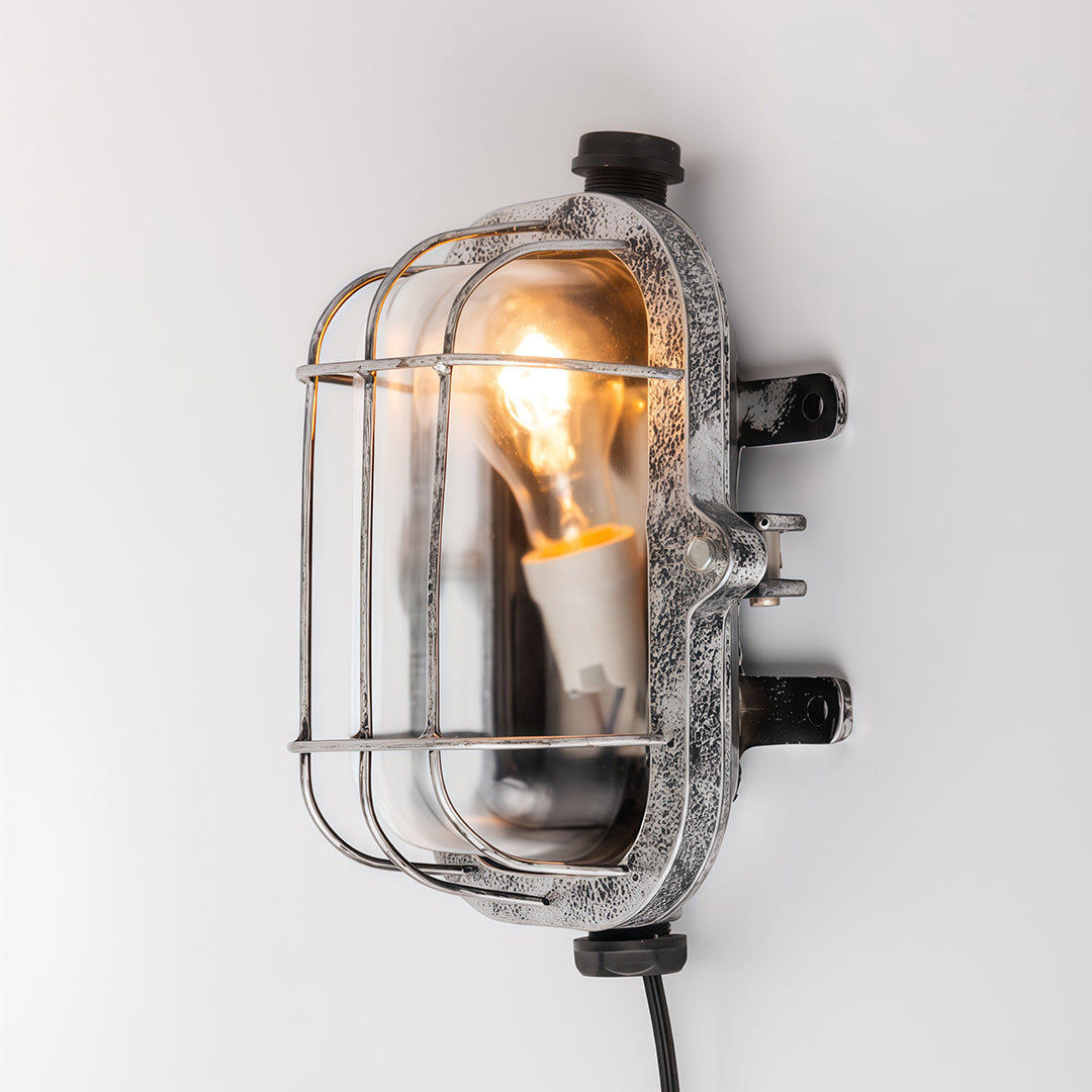 Chrome industrial outdoor sconce with oval cage mounted on white wall showing polished metal finish