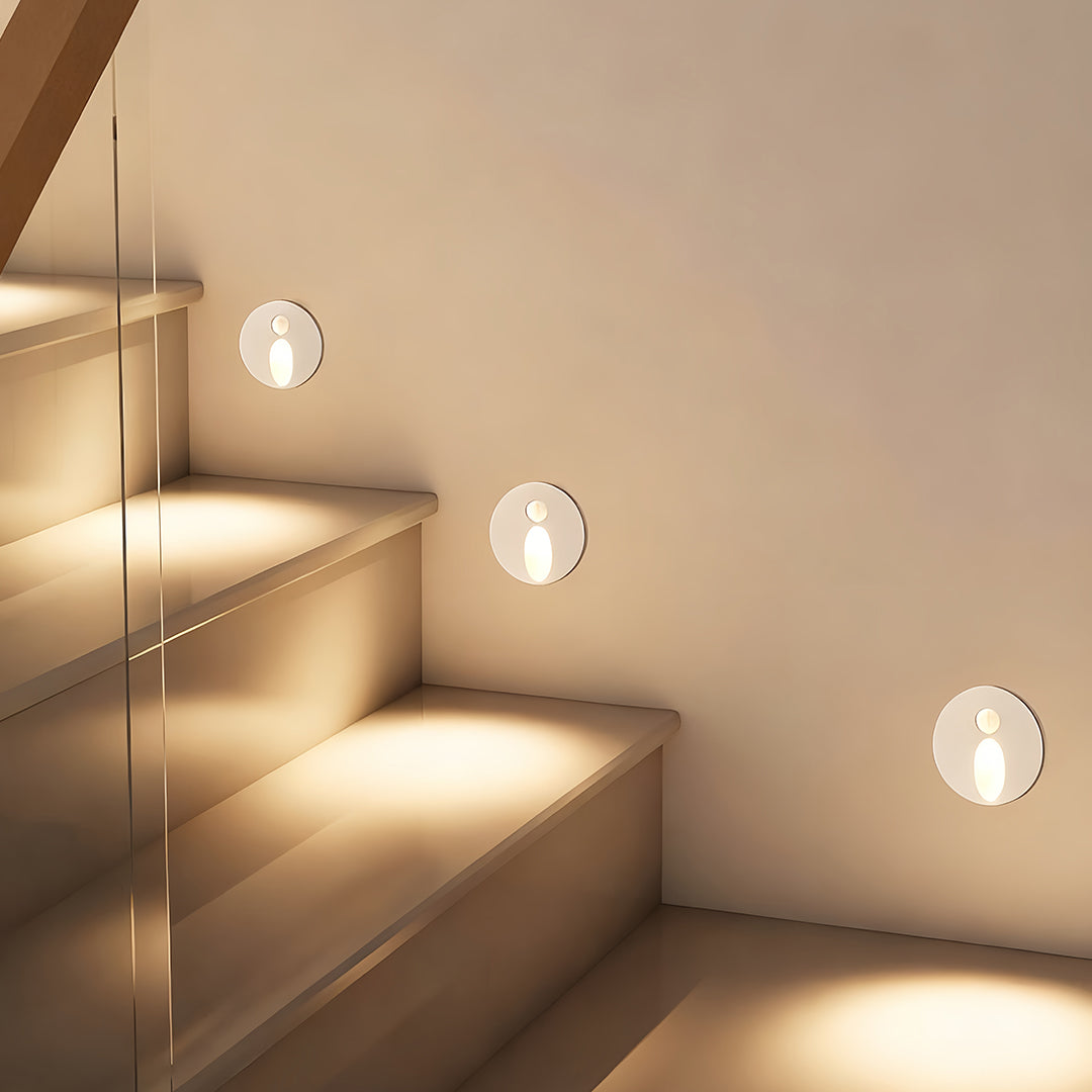 Circular interior stair step lights casting a soft, downward amber glow, highlighting the contemporary floating white marble steps and white wall detail in a modern home.