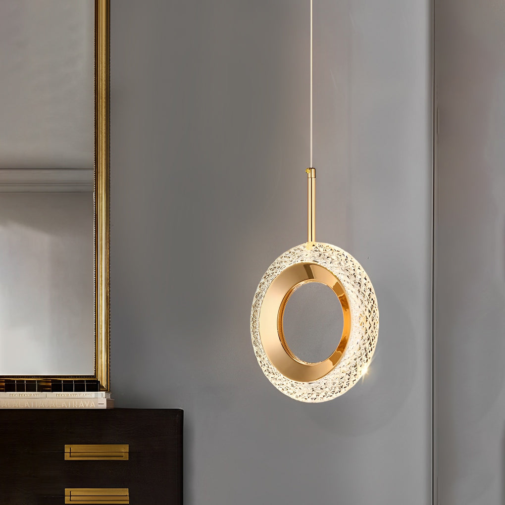 Circular unique pendant light with gold finish hanging near a nightstand.