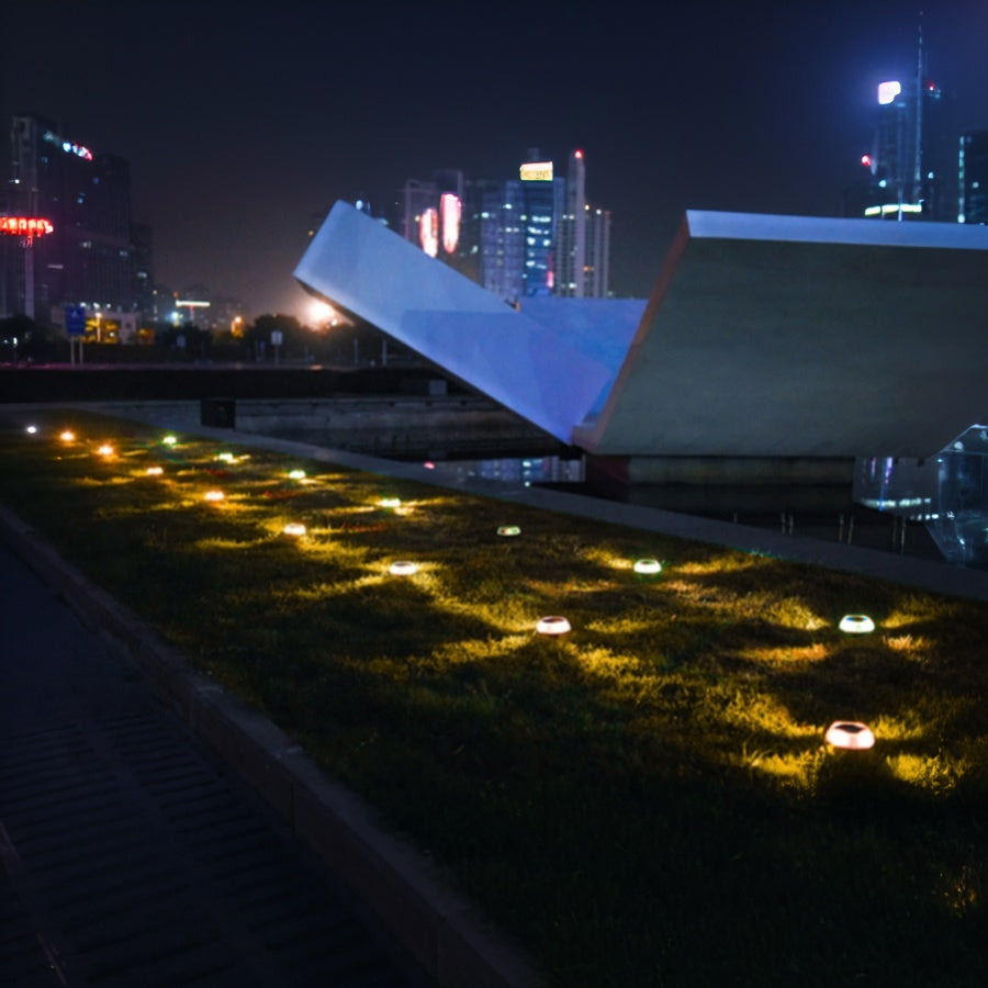 Modern cityscape featuring illuminated pathway with solar ground lights creating dramatic nighttime ambiance