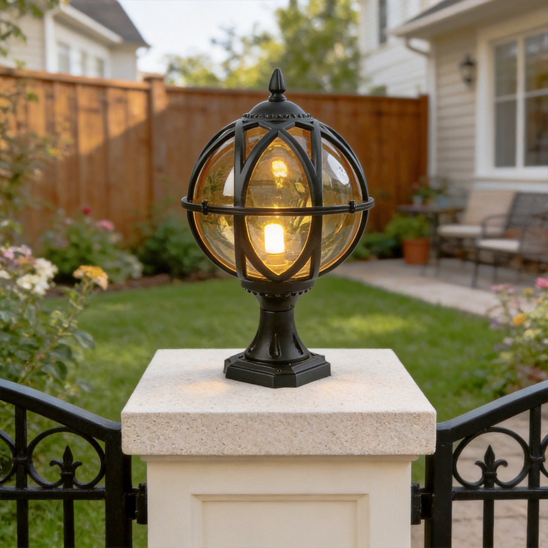 Classic black globe pillar light on white stone post in garden with a wooden fence background.