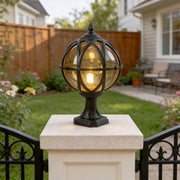 Classic black globe pillar light on white stone post in garden with a wooden fence background.