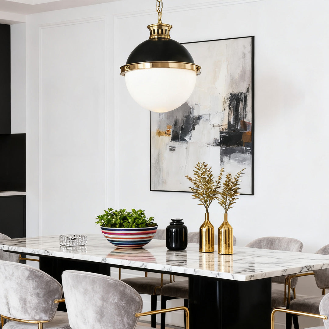 Classic black and gold ball pendant light with an opal glass shade illuminating a modern marble dining table.