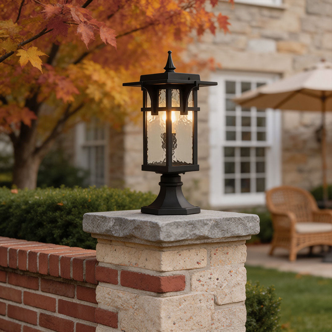 Modern path light with classic black metal frame installed on a brick pillar near autumn foliage.