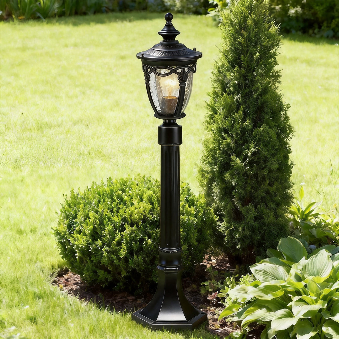 Classic black outdoor light post placed on a bright green lawn surrounded by small green shrubs