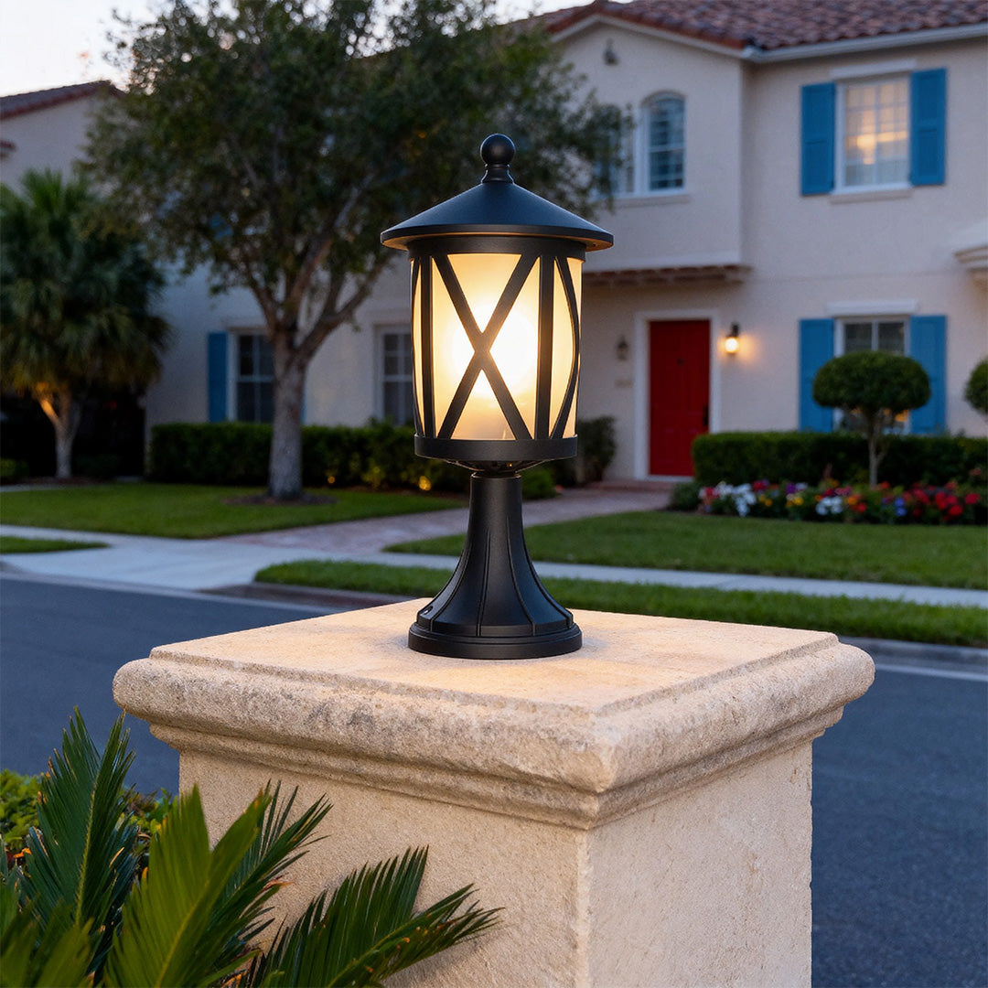 Classic black outdoor pillar light with X-frame design brightening stone pedestal on suburban street at evening