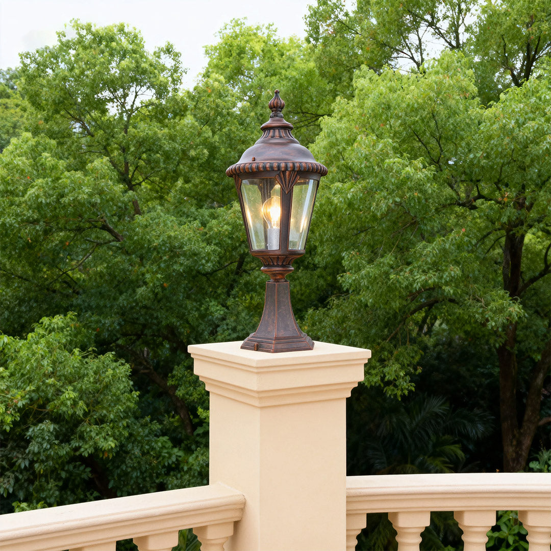 Classic fence pillar light positioned on cream-colored balustrade with lush tree background