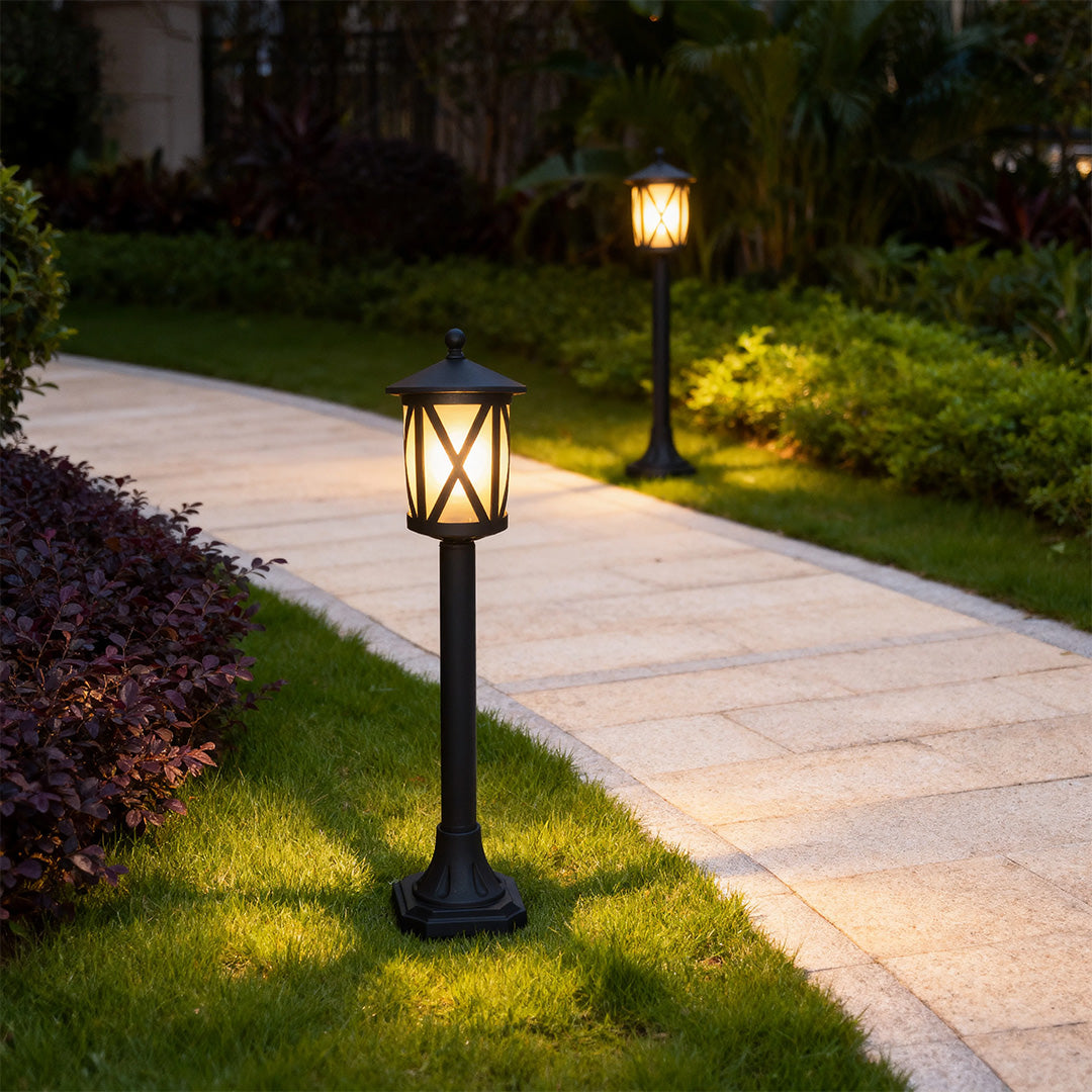 Classic garden bollard light providing ambient lighting along paved path with landscaped borders at dusk