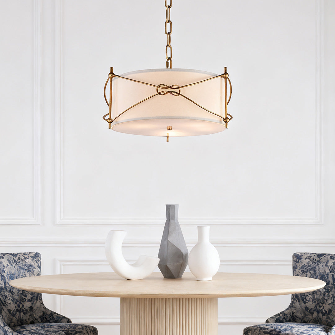 Classic white drum pendant light with exposed gold frame, centered above a simple light wood round dining table and wainscoting.