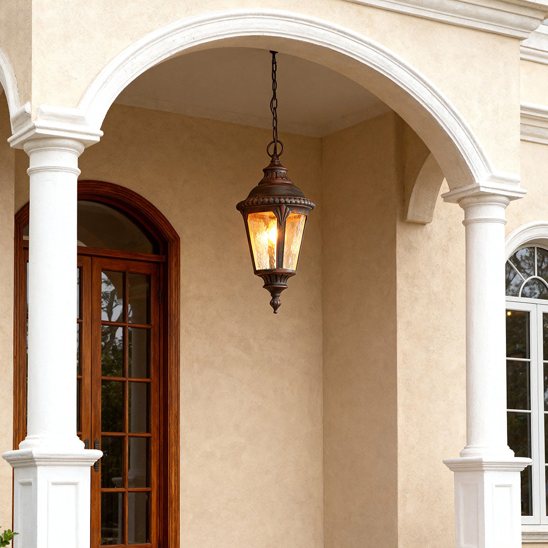 Classic industrial pendant light glowing warmly in arched entryway with stone columns and wooden door