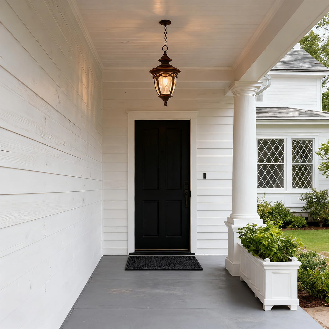Classic pendant porch light brightening white covered entrance with black door and potted plants