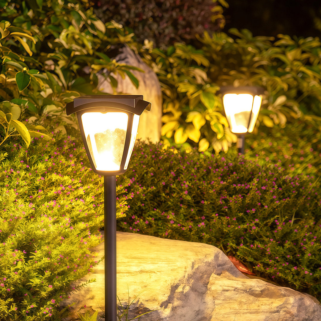 Classic solar powered path lighting lanterns casting a warm, ambient glow in a landscaped rock garden.