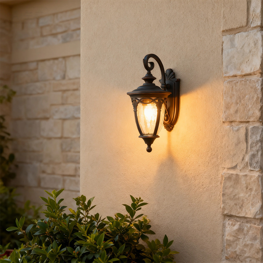 Classic unique outdoor sconce providing ambient lighting on beige stone wall corner with plants