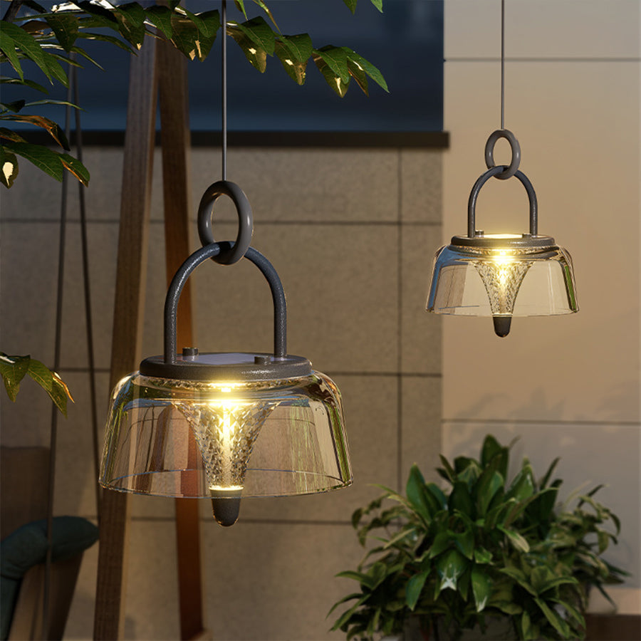 Clear pendant lights with a sleek design, illuminating a garden pathway with soft, golden light.