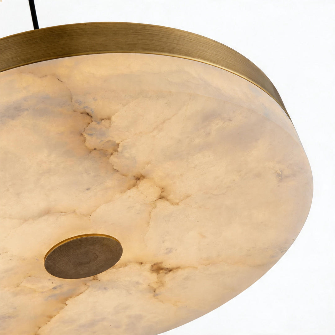 Close up bottom view of a disc pendant light showing warm marble texture and brass center ok.