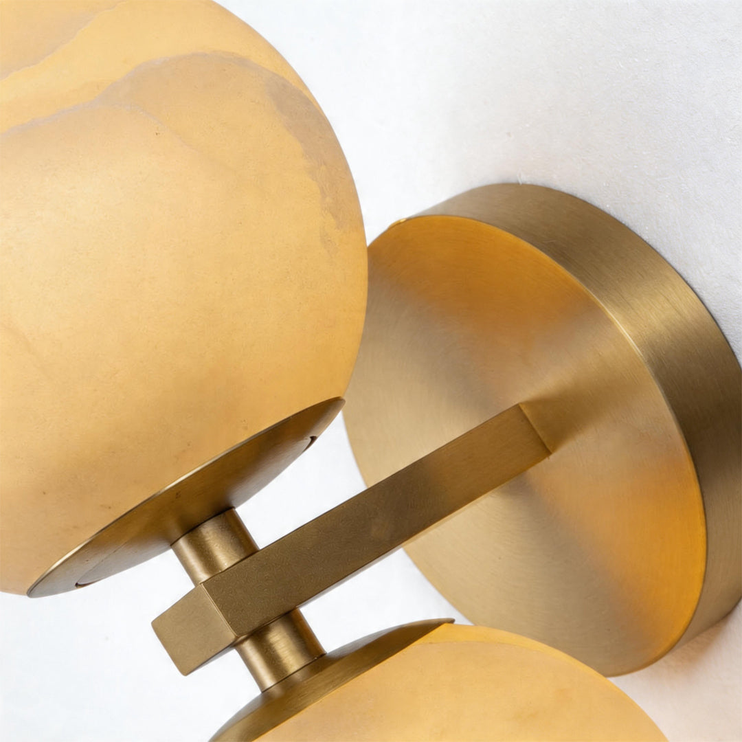 Close up of the brushed brass mounting bracket and stone shades of a modern globe wall light.
