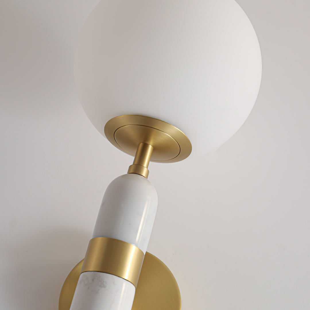 Close up of a gold wall sconce lighting fixture with a white globe and marble stem detail.
