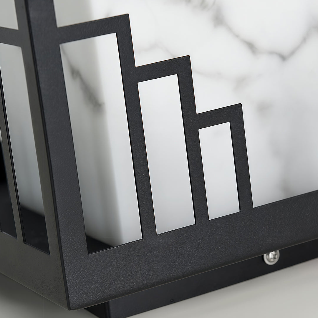 Close-up of outdoor pillar light featuring glass shade chandelier design highlighting architectural cityscape pattern in metal frame.