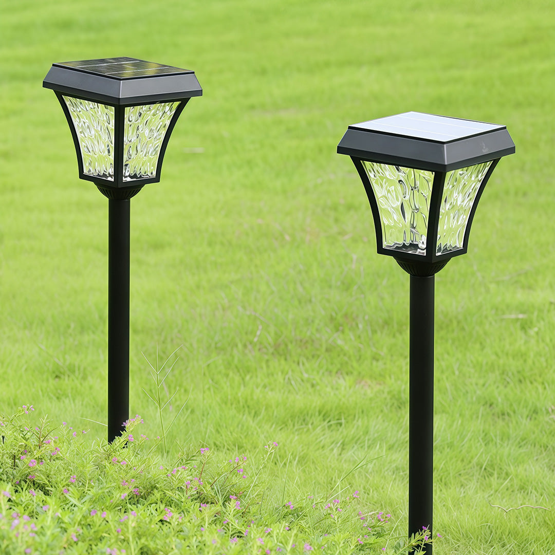 Close-up product shot of two outdoor solar path lighting fixtures with textured glass, staked in a green lawn.